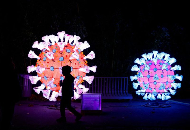 A visitor walks past an illuminated coronavirus (COVID-19) model as he visit the "Mini-Worlds on the Way of Illumination" (Mini-Mondes en voie d'illumination) exhibition during the Light Festival preview at the Jardin des Plantes (Botanical garden) in Paris, France, November 12, 2022. REUTERS