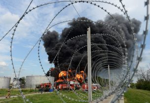 A view through barbed wires show smoke from fire rising above a burning fuel tank of an oil depot in Voronezh, Russia, June 24, 2023. REUTERS/Stringer