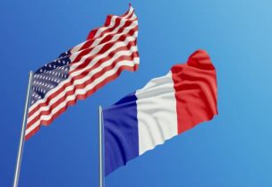 American and French flags are waving with wind over blue sky