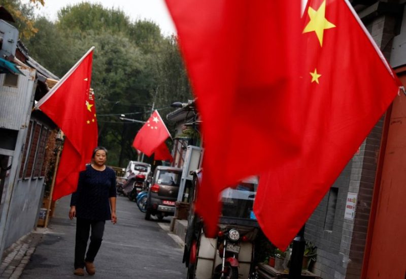 A woman walks through a hutong alley hung with Chinese national flags, ahead of the 20th National Congress of the Communist Party of China, in Beijing, China October 14, 2022. REUTERS