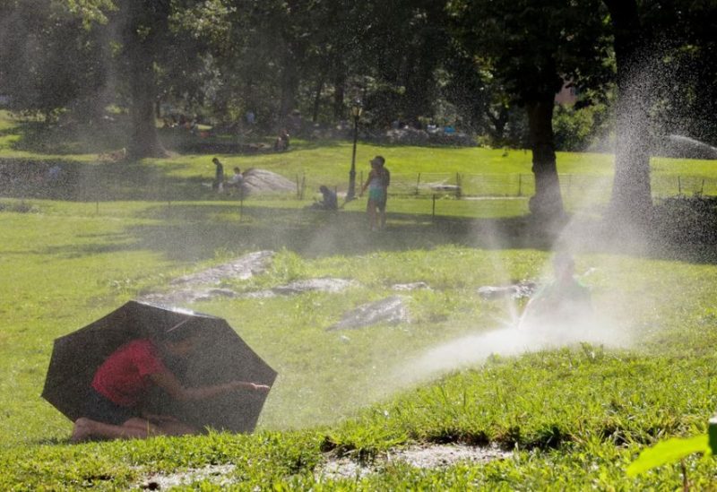 A child takes shelter under an umbrella while another one plays with a water sprinkler, in Manhattan's Central Park, in New York City, U.S., July 28, 2023. REUTERS