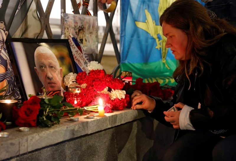 A woman lights a candle in front of a portrait of Wagner mercenary chief Yevgeny Prigozhin at a makeshift memorial in Moscow, Russia August 24, 2023. REUTERS/Stringer