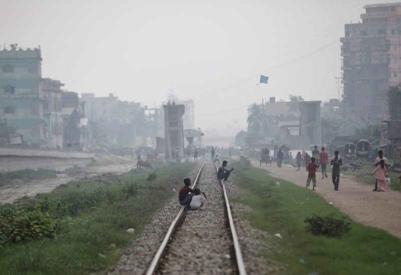People sit on a rail track as smoke rises from steel mills near a slum in Dhaka, Bangladesh, August 29, 2023. REUTERS/Mohammad Ponir Hossain