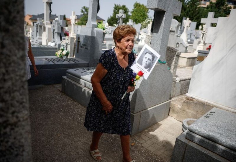 Benita Navacerrada Lopez walks as she holds a picture of her father Facundo Navacerrada Perdiguero who was one of the people who were killed by the forces of dictator Francisco Franco and for whom members of the Aranzadi Science Society are searching for in a mass grave in the Colmenar Viejo cemetery, Spain, August 9, 2023. REUTERS/Juan Medina
