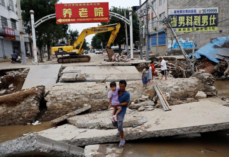A man holding a child walks across a damaged bridge after the rains and floods brought by remnants of Typhoon Doksuri, in Zhuozhou, Hebei province, China August 7, 2023. REUTERS