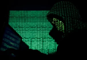A hooded man holds a laptop computer as cyber code is projected on him in this illustration picture taken on May 13, 2017. REUTERS