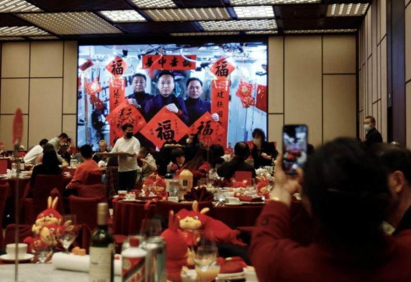 :A woman takes pictures of a screen displaying the Spring Festival greetings by Chinese astronauts Fei Junlong, Deng Qingming and Zhang Lu from China's space station, during a Lunar New Year's Eve dinner service at Shangri-La Shougang Park hotel in Beijing, China, January 21, 2023. REUTERS