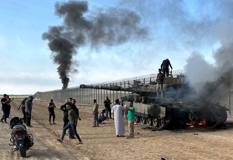 Palestinians react as an Israeli military vehicle burns after it was hit by Palestinian gunmen who infiltrated areas of southern Israel, at the Israeli side of Israel-Gaza border, October 7, 2023. REUTERS/Mohammed Fayq Abu Mostafa NO RESALES. NO ARCHIVES.