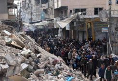 Crowds of locals and displaced Palestinians walk past destroyed buildings in the southern Gaza Strip city of Khan Yunis on November 28, 2023