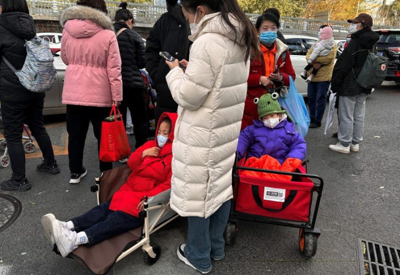 People stand next to children sitting in camping carts as they wait for their rides outside a children's hospital in Beijing, China November 27, 2023. REUTERS/Tingshu Wang