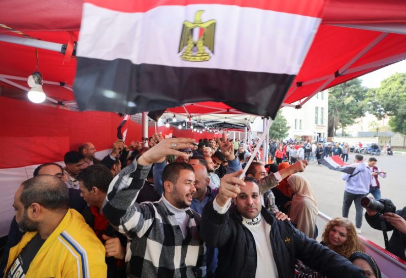 A man waves Egypt's national flag as people wait in line outside a polling station to vote during the first day of the presidential election in Cairo, Egypt, December 10, 2023. REUTERS/Mohamed Abd El Ghany