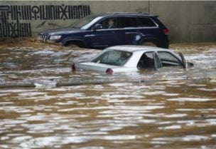 A man, background, drives his car in front a car submerged in flood water at a highway flooded by the rains, in Beirut on Dec. 23, 2023. (AP)